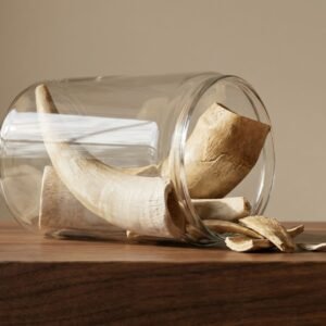 Clear glass jar tipped on its side spilling dried banana peels onto a wooden table. The peels curve inside and spill out.”,