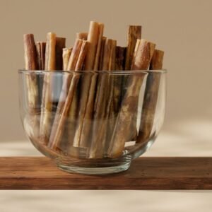 Glass bowl filled with cinnamon sticks resting on a wooden board, warm neutral background