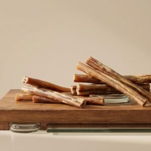 Cinnamon sticks piled on a wooden cutting board with a glass plate beneath, against a beige background.