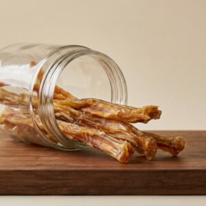 Dried beef jerky sticks spilling from a glass jar onto a wooden table
