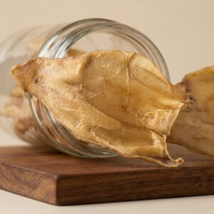 Close-up of a wrinkled, dried beige food sheet spilling from a glass jar onto a wooden board.