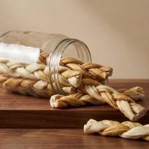 Twisted breadsticks spilling from a glass jar onto a wooden surface.