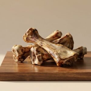 Pile of large beef marrow bones on a wooden cutting board in a simple setting.
