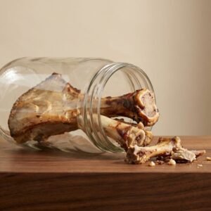 Bones with marrow spilling from a tipped glass jar onto a wooden cutting board.
