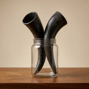 Three dark horn-like objects arranged inside a clear glass jar on a wooden table.