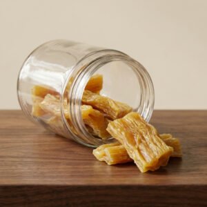 Dried fruit chunks spilling from a glass jar onto a wooden tabletop.