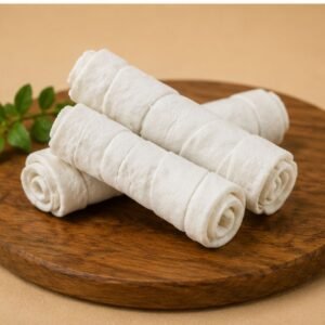 Stack of white rolled wafer cookies on a round wooden board, with a small green herb in the background