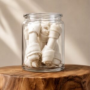 Clear glass jar filled with rolled white cloths, arranged like small scrolls, sitting on a wooden surface.