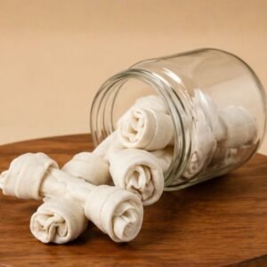Rolled white cloth napkins shaped like roses spilling from a glass jar onto a wooden table.